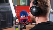 Blick von hinten auf unseren Moderator Sascha Sommer, der im neu umgebauten NDR 2 Studio am Mikrofon steht. © NDR 2 Foto: Niklas Kusche